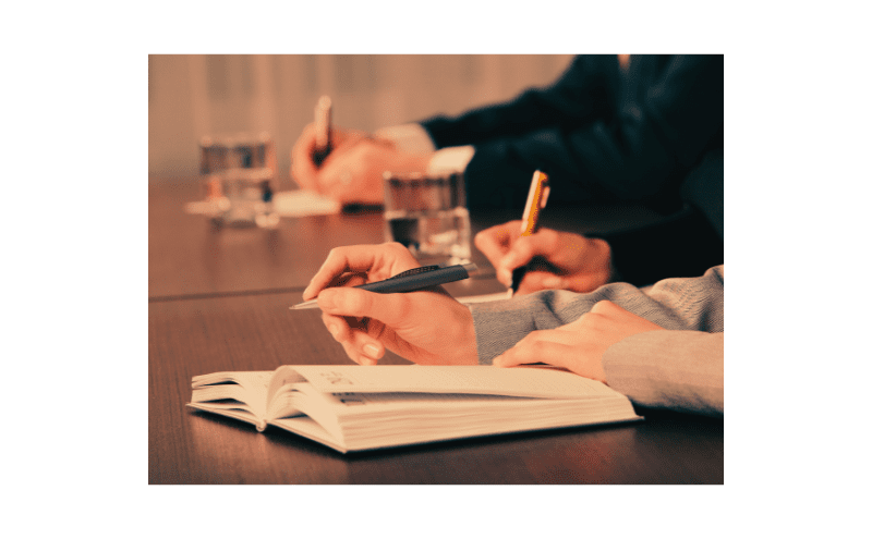 Winning With Writing Workshop People participating in a Writing Workshop. Hands with pens and paper all focused on a tabletop.