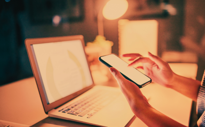mary-moss-digital-downloads-header-image-left-column Social Media Mastery An open laptop and someone's arms, the hands are holding a cellphone and scrolling. The screens are lit up, but you can't see what is on them, they are out of focus.