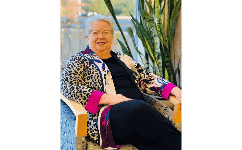 mary-moss-seated-author-portrait Author Mary Moss seated comfortably in a lounge area, smiling toward the camera.